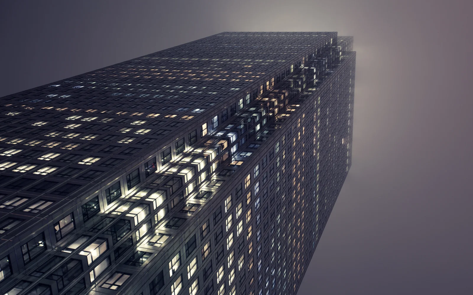 一座布满发光窗户的高层建筑从低角度延伸向夜空。