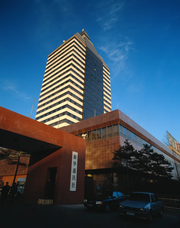 一座高层建筑矗立在晴朗的蓝天下，前景是低层城市建筑和停放的汽车。