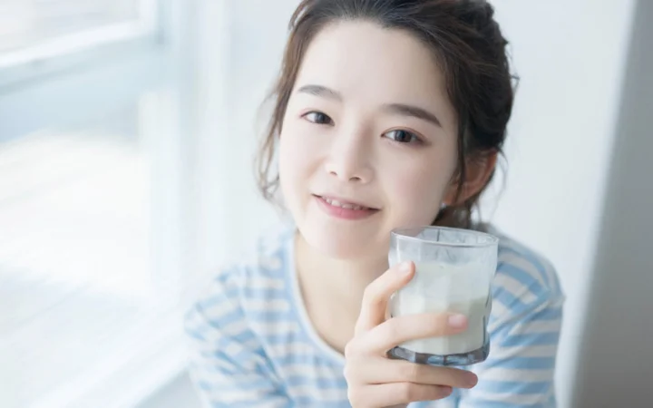 一名面带微笑的女子在明亮的窗边手持一杯牛奶。