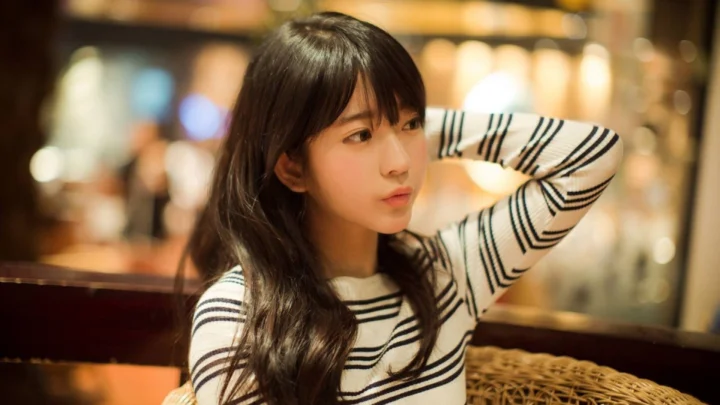 一名长发女性穿着黑白条纹衫坐在温暖灯光的室内环境中。