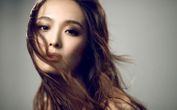 一名成年女性的近距离肖像，长发随意垂落在脸侧，背景为柔和的灰色。