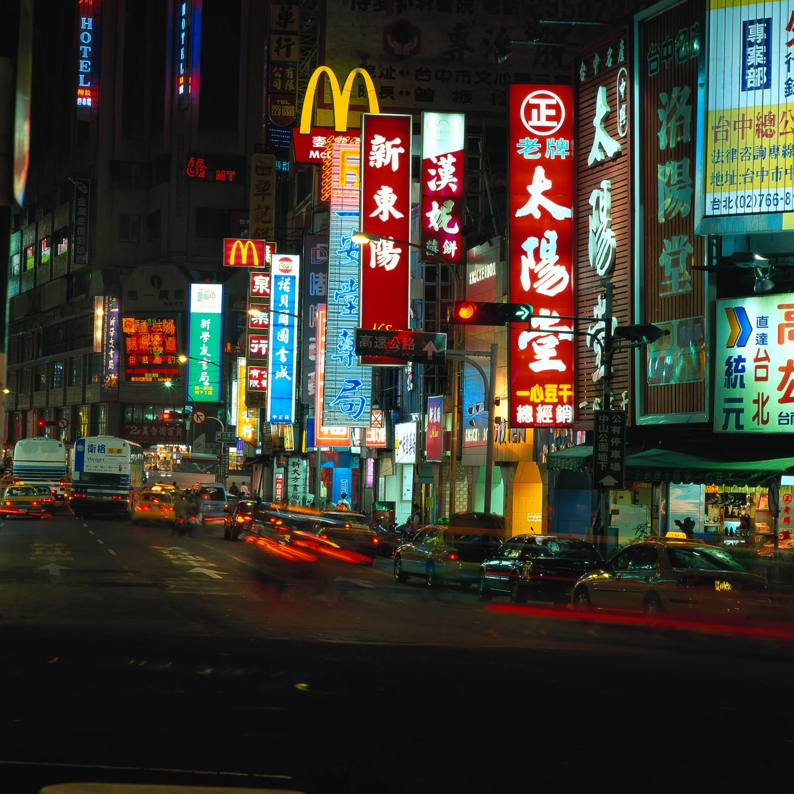 夜晚繁华街道两旁布满霓虹招牌，车辆在街面上流动。