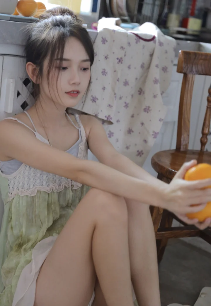 한 여성이 실내에 앉아 오렌지에 손을 뻗고 있다.