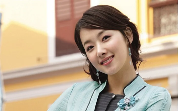 귀걸이를 하고 연한 초록색 재킷을 입은 미소 짓는 여성의 실내 인물 사진입니다.
