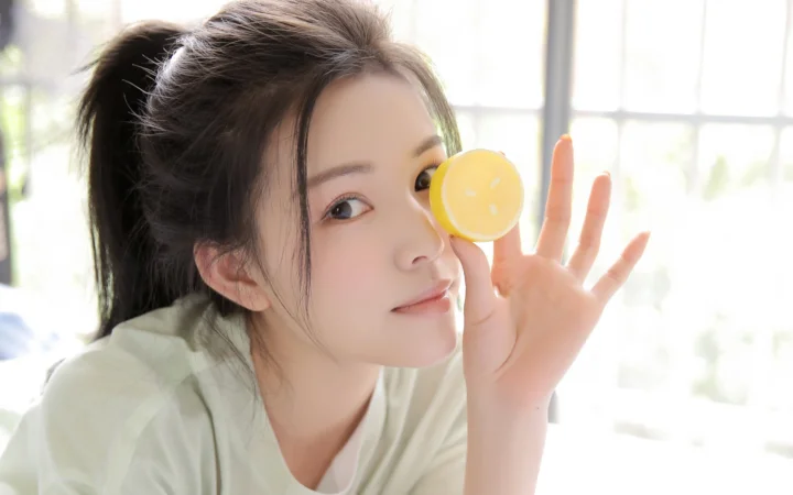 一位女性在明亮窗边手持黄色柠檬微笑看向镜头。