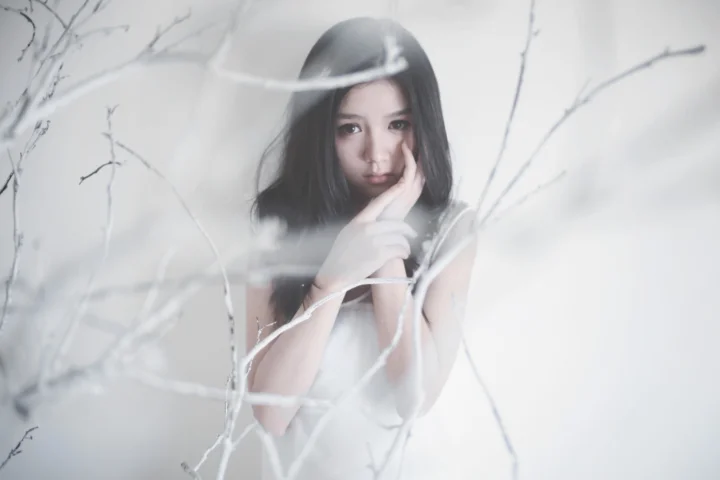 一名穿白衣的女性置身于朦胧的白色枝条之间，呈现柔和清冷的人像画面。