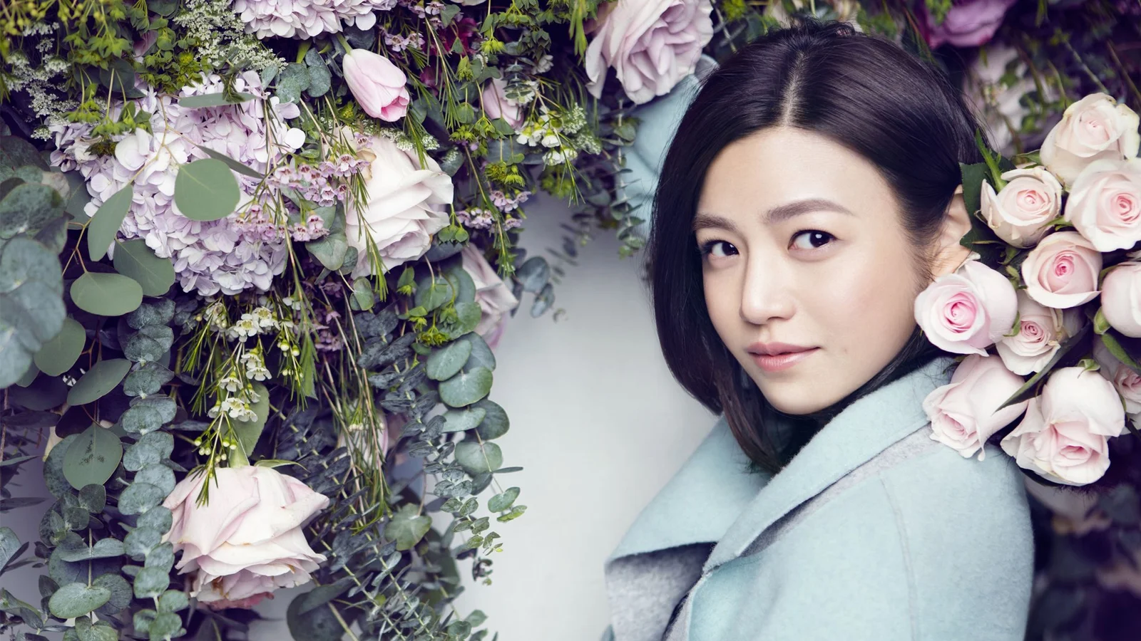 一名成年女性置身于粉白色花朵与绿叶之间。