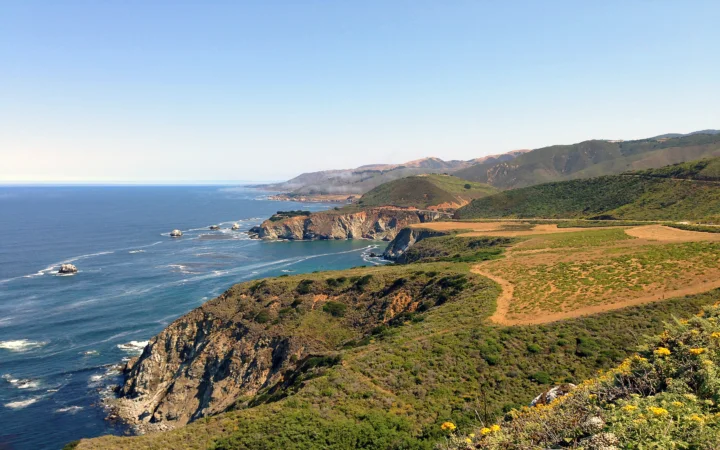晴朗天空下，海岸悬崖、蓝色海面与起伏丘陵构成开阔的自然景观。