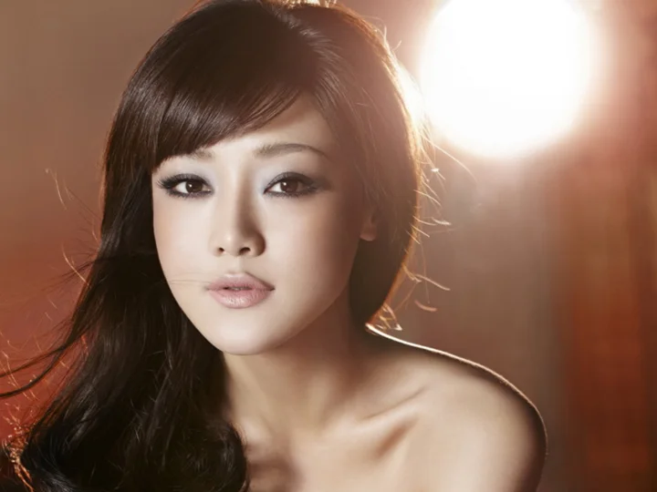 따뜻하고 부드러운 빛 아래 긴 검은 머리를 한 성인 여성이 카메라를 바라보고 있습니다.