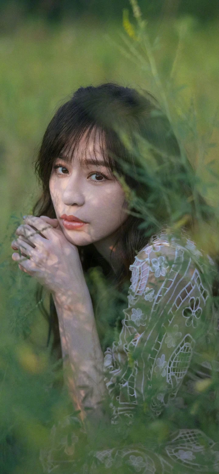 一位成年女性被绿叶掩映，身穿蕾丝上衣，呈现自然的人像构图。