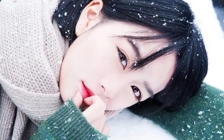 一名穿着针织衫的成年女性躺在雪地中，脸旁和头发上落着雪花。