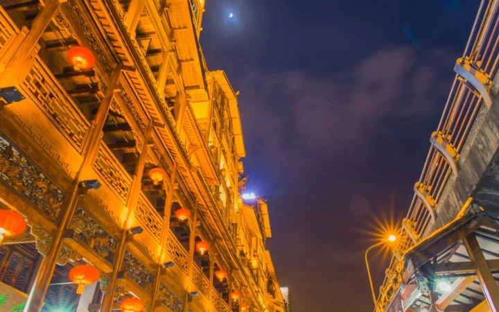 夜色中的传统木质建筑挂满红灯笼，街灯映照着两侧建筑与深蓝色天空。