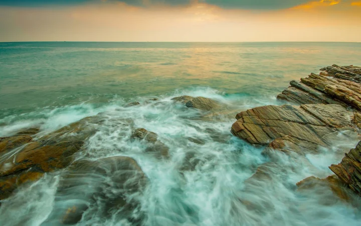 夕阳映照下，海浪在岩石海岸间翻涌。