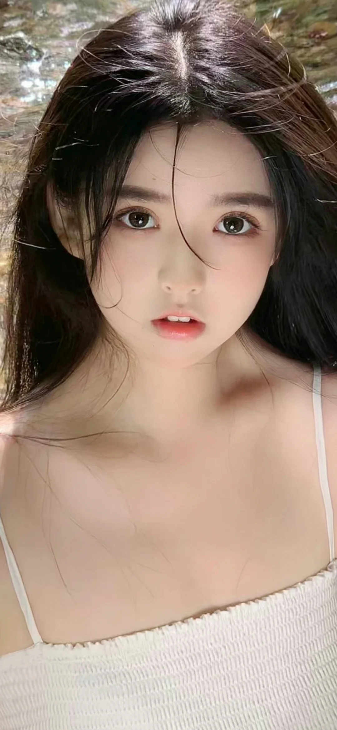 一位长发女性在户外水边近距离面对镜头，画面以她的面部和上半身为主体。