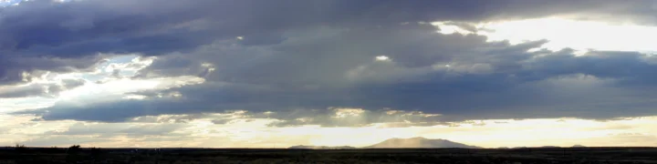 厚重云层下的夕阳照亮了地平线与远处山脉。
