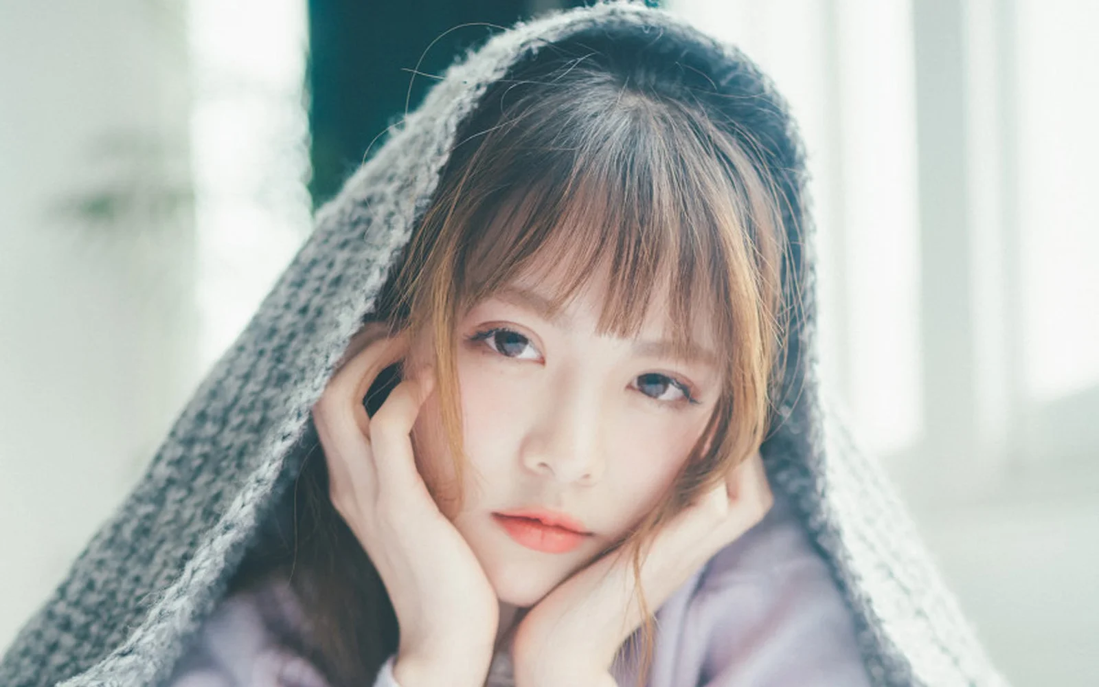 一名女性在柔和室内光线下裹着灰色毯子直视镜头。