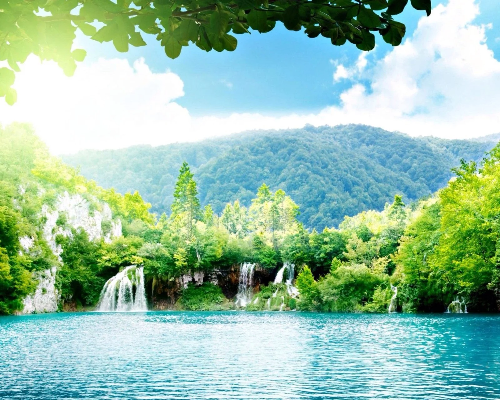 碧蓝湖水前方分布着瀑布、森林和远山，树叶从上方形成自然框景。