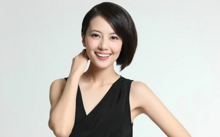 黒いノースリーブの服を着た成人女性が、明るい背景の前で微笑んでいる。