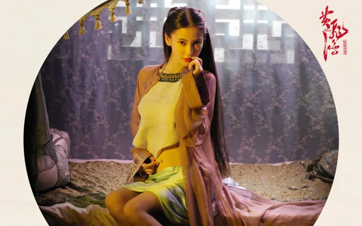 一名穿着连衣裙的女性坐在室内床边，背景带有柔和光影。