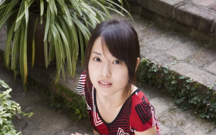 一名女子站在庭院植物旁，面向镜头微笑。