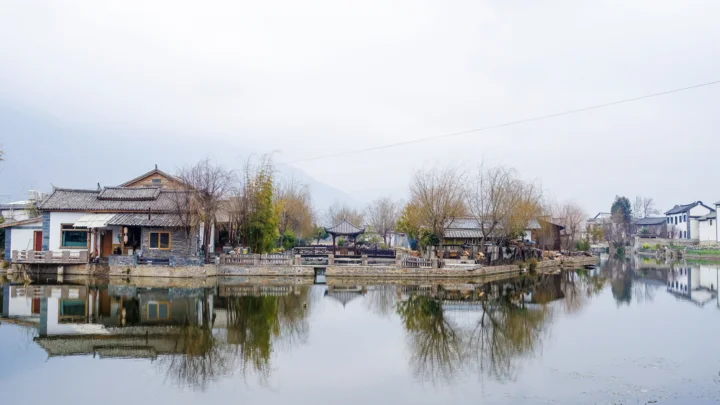 湖畔村落、树木与传统建筑倒映在平静的水面上。