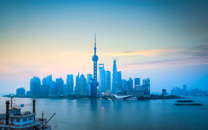 暮色中的城市天际线横跨江面，中央矗立着高耸的电视塔，前景可见一艘小船。