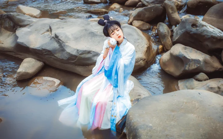 一名身穿传统服饰的女子坐在溪流岩石之间。