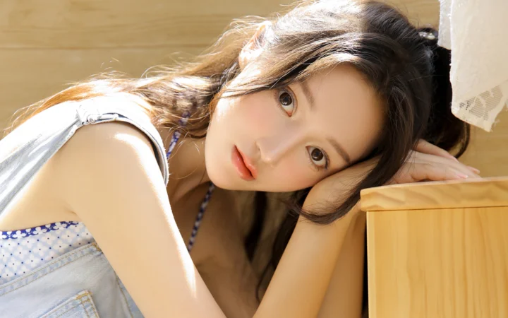 성인 여성이 햇살이 비치는 실내에서 나무 가구에 기대어 누워 있다.