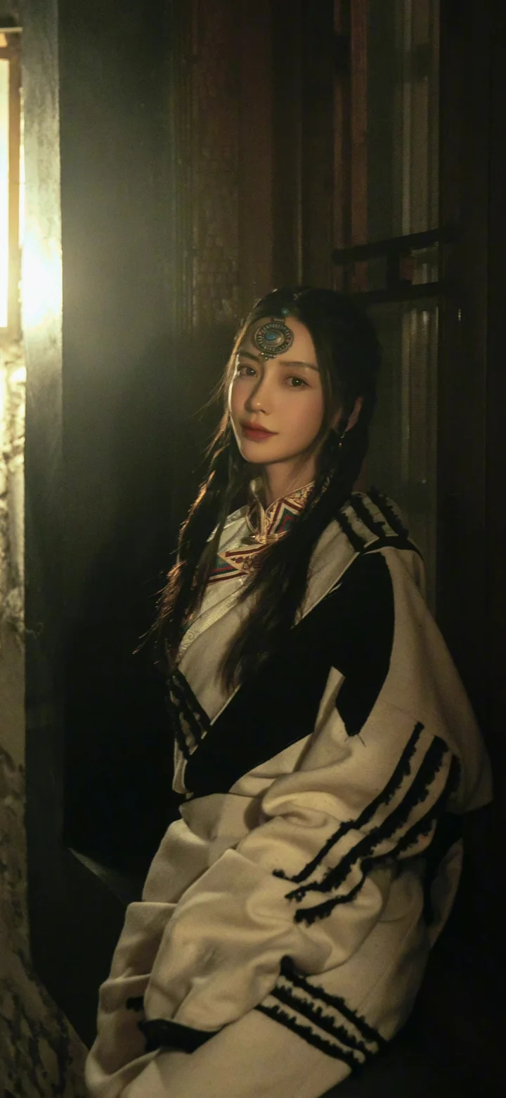 一名身穿传统服饰的成年女性在室内暖光下靠墙坐着。