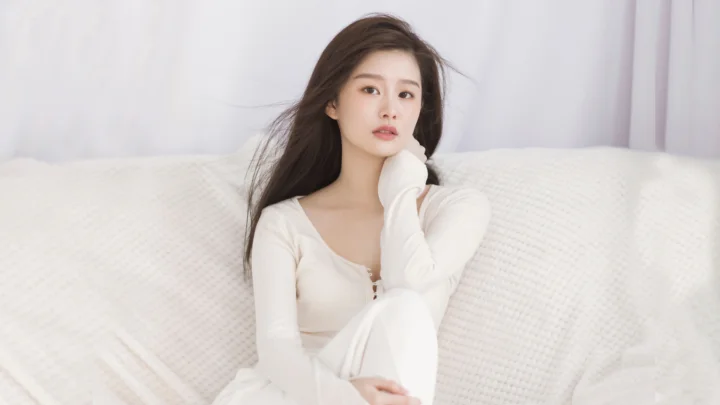 一名成年女性坐在白色沙发上，背景是浅色窗帘。