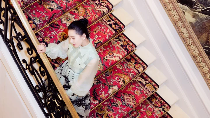 一位女士站在铺有红色图案地毯的室内楼梯旁。