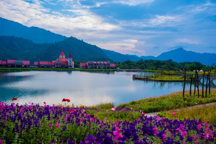 湖泊、群山、湖畔建筑与盛开的花田构成宁静的山地风景。