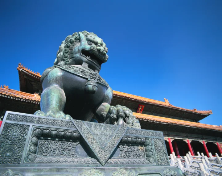 一尊威严的石狮雕像矗立在金色屋檐与蓝天下方。