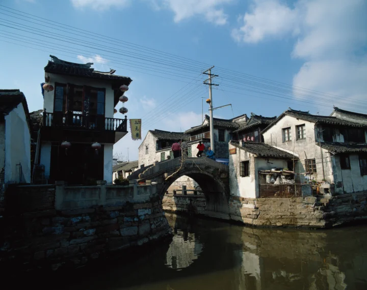 古镇石拱桥横跨宁静水巷，两岸是传统民居，天空中可见电线与白云。