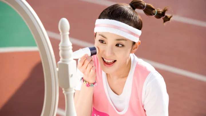 성인 여성이 운동장 옆에서 거울을 보며 화장을 하고 있습니다.