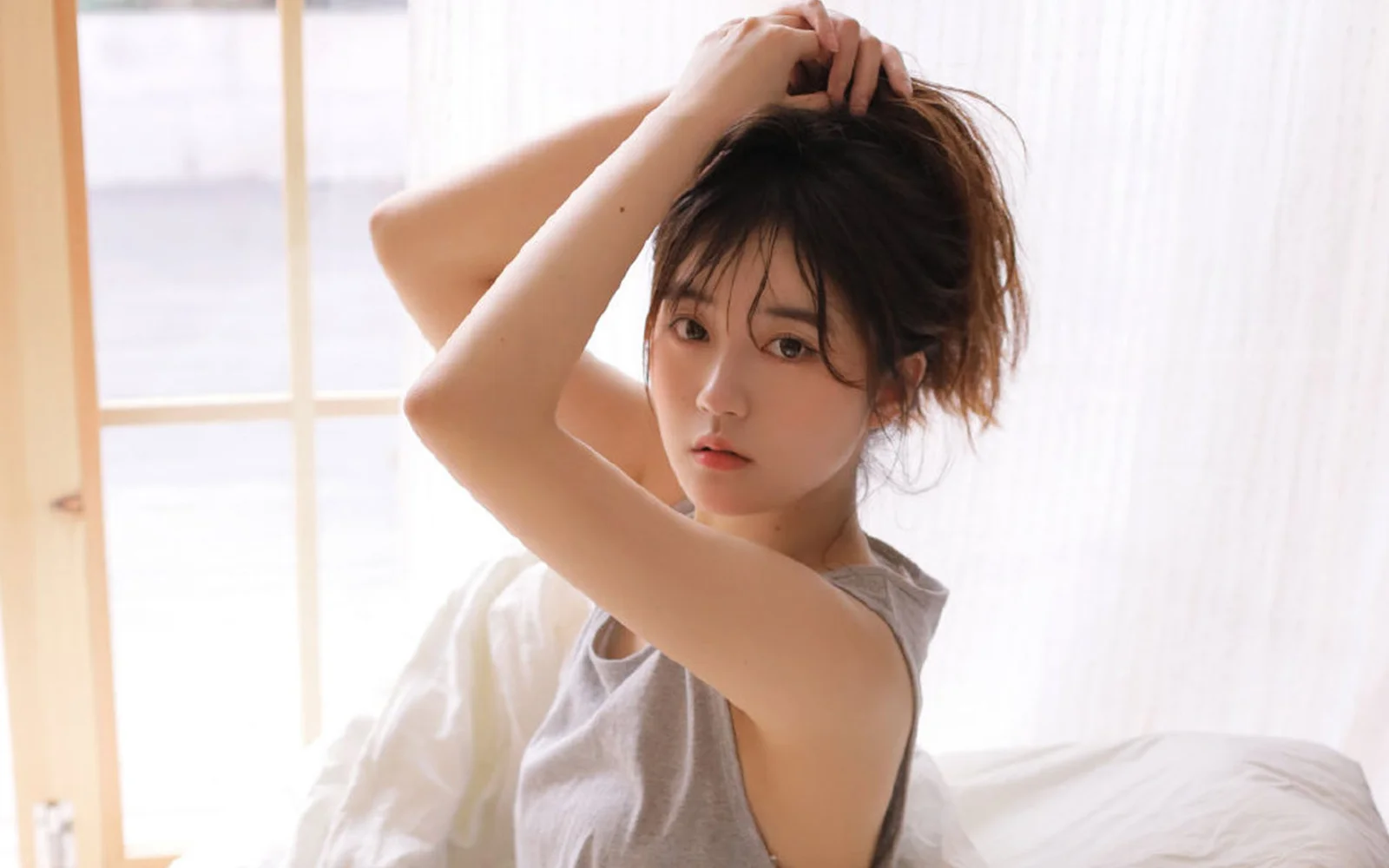 밝은 침실 창가에서 머리를 정리하는 성인 여성.