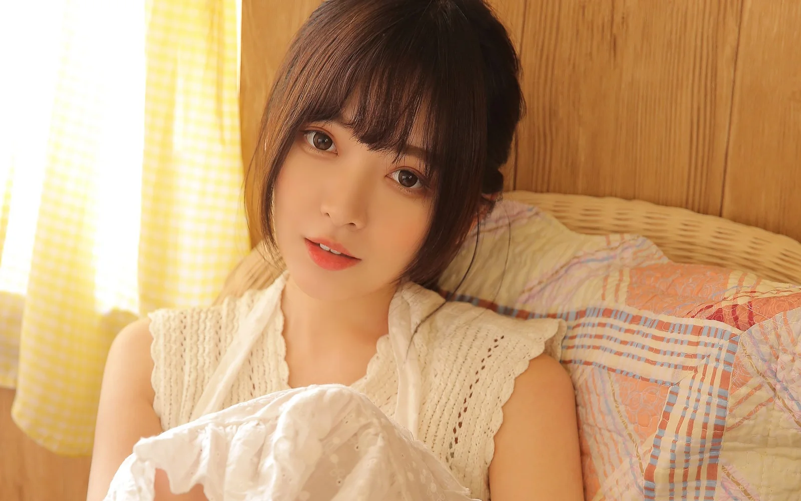 女性が寝室のベッドに座り、窓から差し込む暖かな光が顔を照らしている。