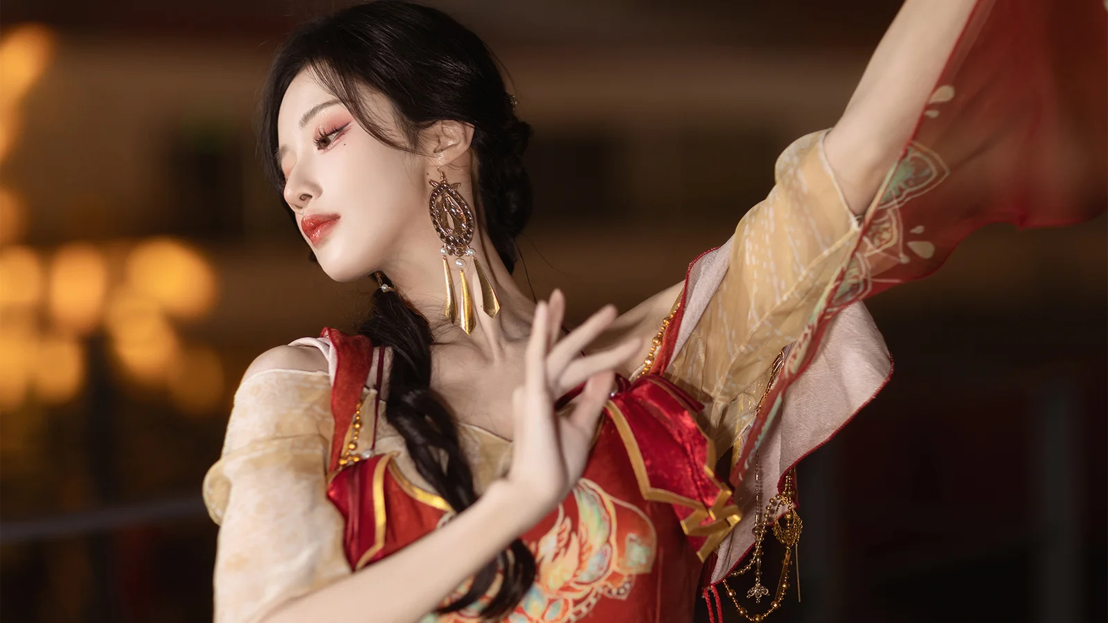 붉은 전통 의상을 입은 성인 여성이 따뜻한 실내 배경 앞에서 춤 동작을 취하고 있다.