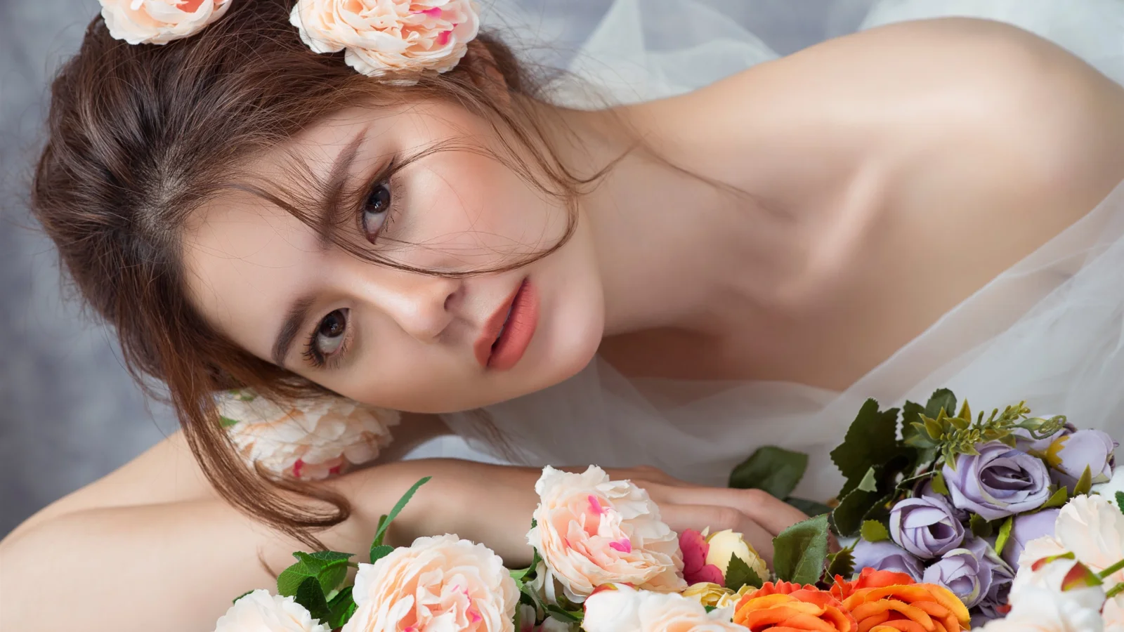 꽃 사이에 누워 있는 성인 여성을 부드러운 분위기로 담은 인물 사진입니다.