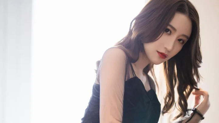 一名成年女性在明亮窗边侧身面对镜头，身穿黑色上衣。