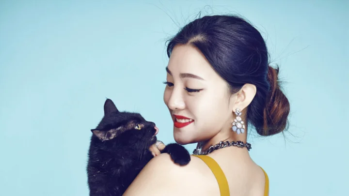 一名女子抱着黑猫，在浅蓝色背景前微笑凝视它。