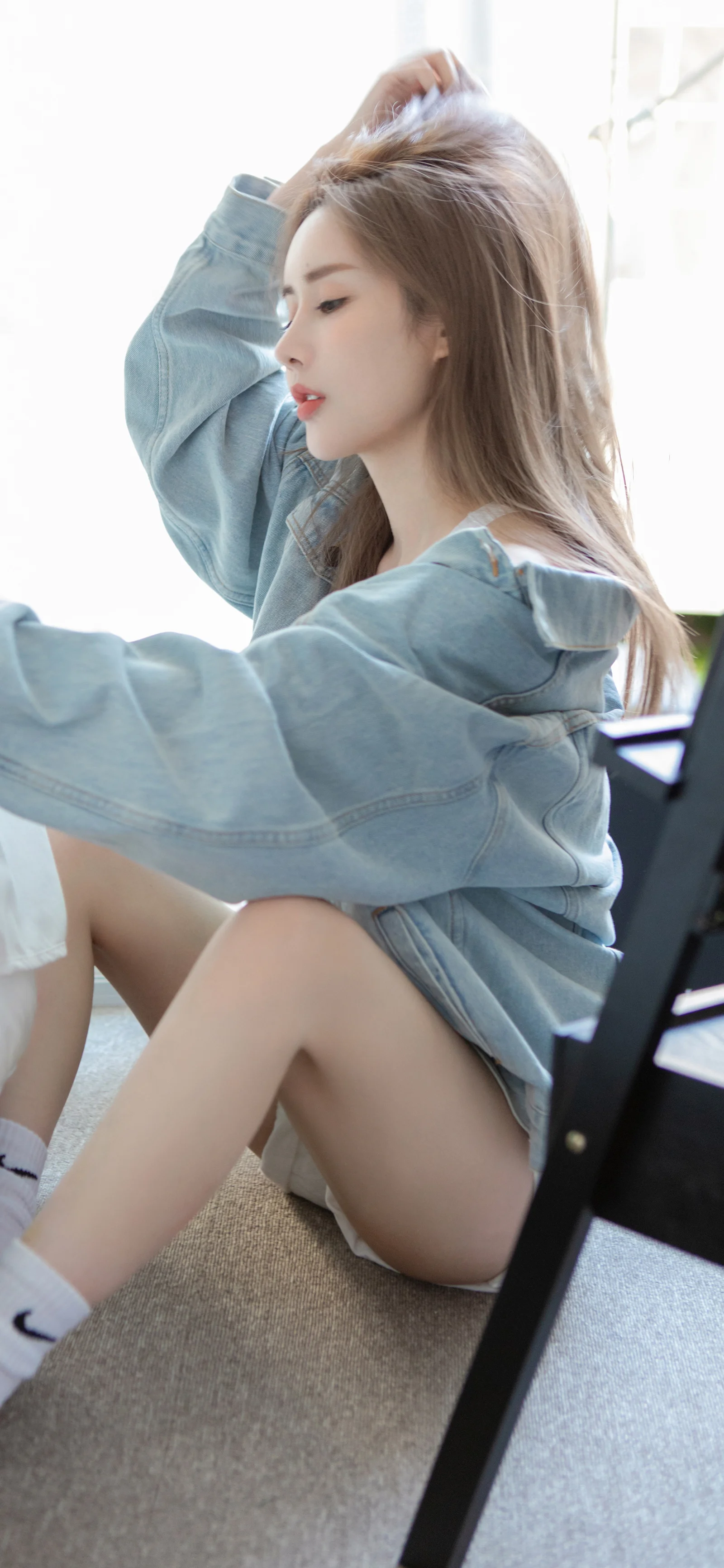 淡いデニムジャケットを着た成人女性が室内の床に座っています。