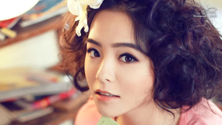 画面中是一位佩戴白色花饰、留着卷发的成年女性近距离肖像。