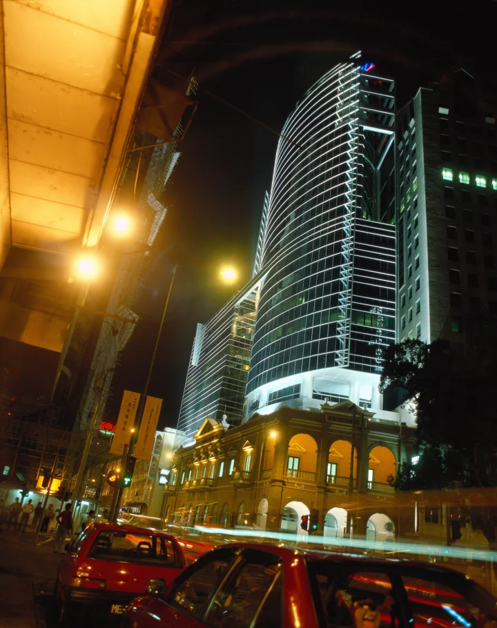 夜色中的现代曲线高楼与古典建筑并立，街道上车流经过。