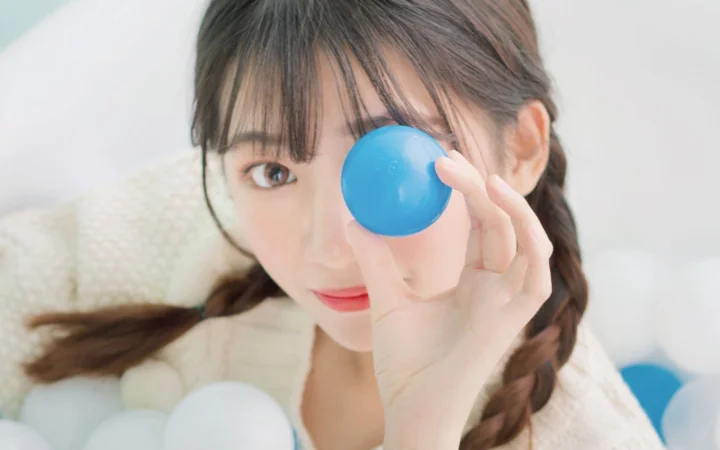 一名女性手持蓝色球遮住一只眼睛，近距离面对镜头。