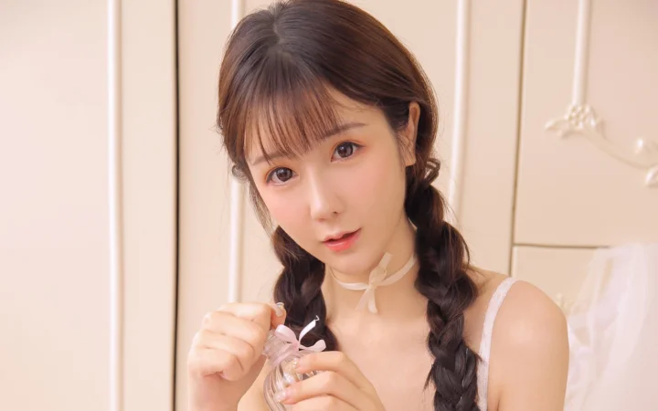 一位留着双辫的女性在暖色室内对着镜头微笑。