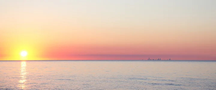 夕阳落在平静海面上，柔和的粉橙色天空映照出金色水面倒影。