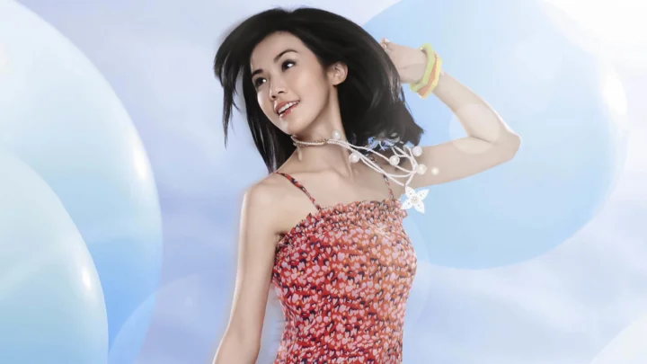 一名成年女性身穿彩色花卉吊带裙，在浅蓝色和白色的柔和背景前摆姿势。
