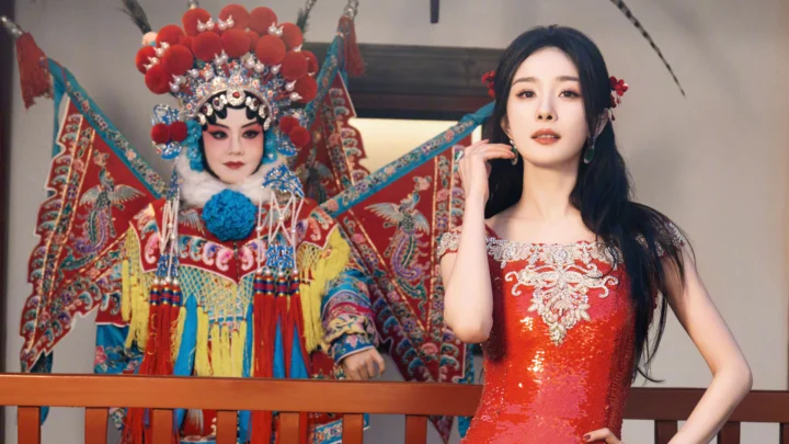 一名身穿红色亮片礼服的女子站在一位身着华丽戏曲服饰的表演者旁边。