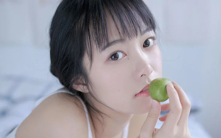 一位女性近距離手持綠色水果靠近嘴唇。